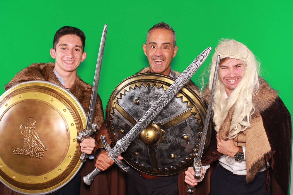 three men posing with medieval swords and shields on a green screen backdrop
