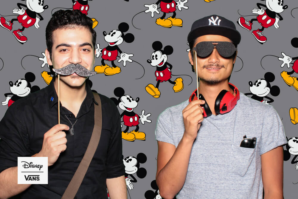 two men posing with props in front of a mickey mouse backdrop