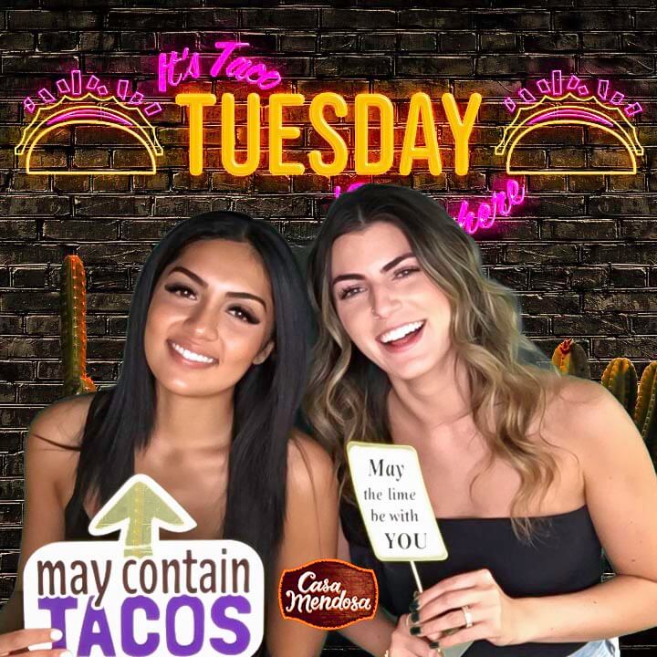 two women posing at a taco and tequila event while holding custom photo booth signs