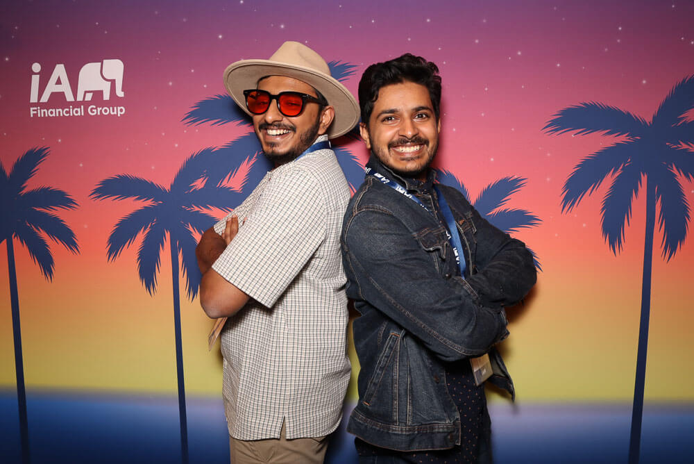 Two men posing in front of a custom printed backdrop with palm trees