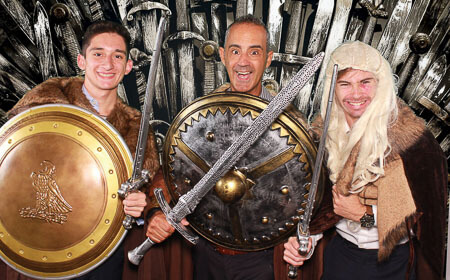 three men posing with swords and shields in a photo booth