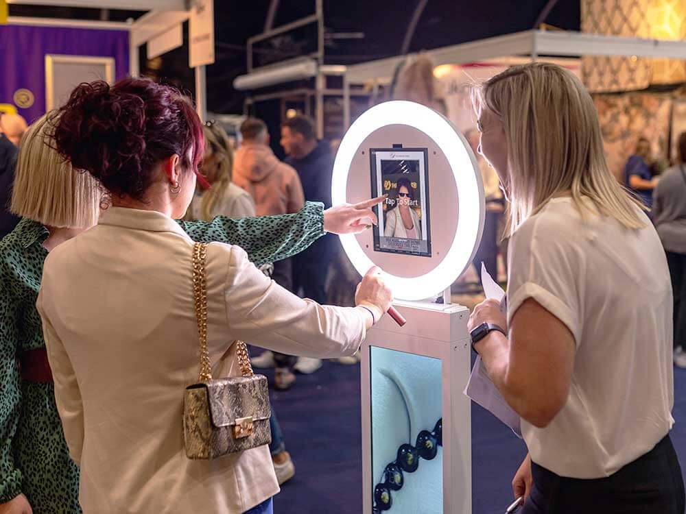 Two ladies looking at a photo booth image on the screen of a photo booth at a trade show