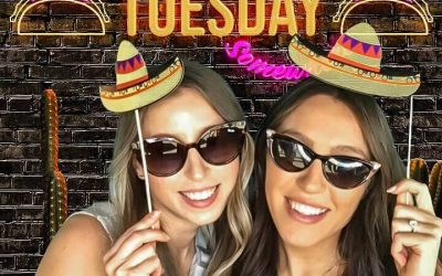 Two women posing with fun prop hats in a Taco Tuesday photo booth in Toronto